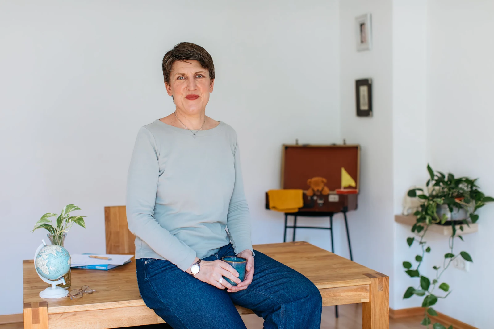 Angela Harde, Gründerin von Senior Aupair, in einem hellen Raum mit Globus und Reisekoffer.